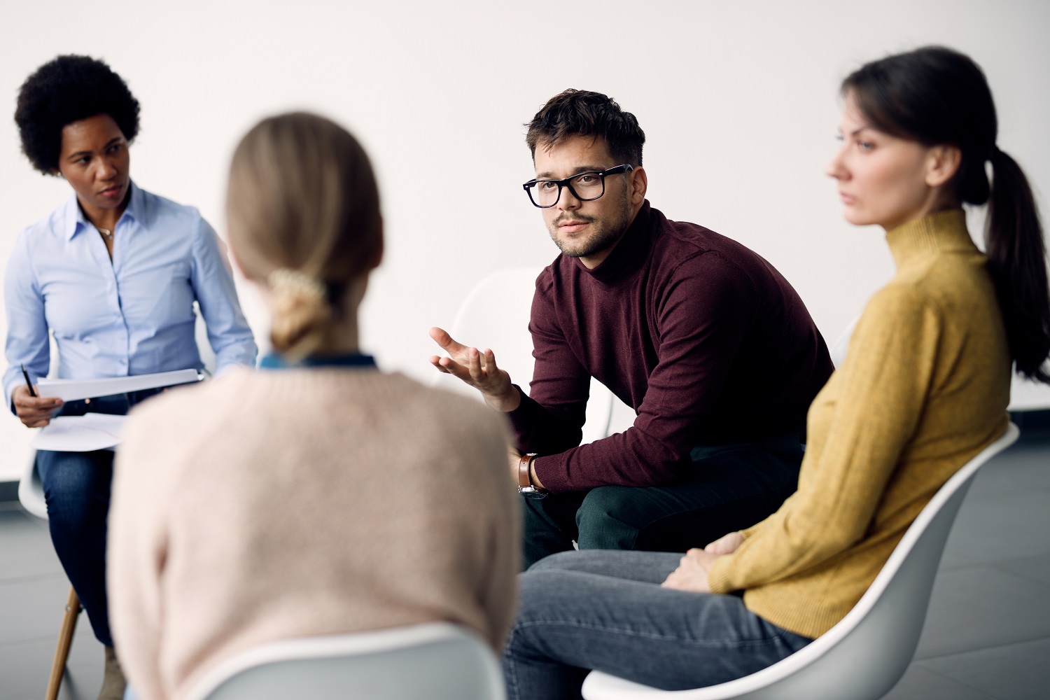 Young man communicating with participants of group therapy at co